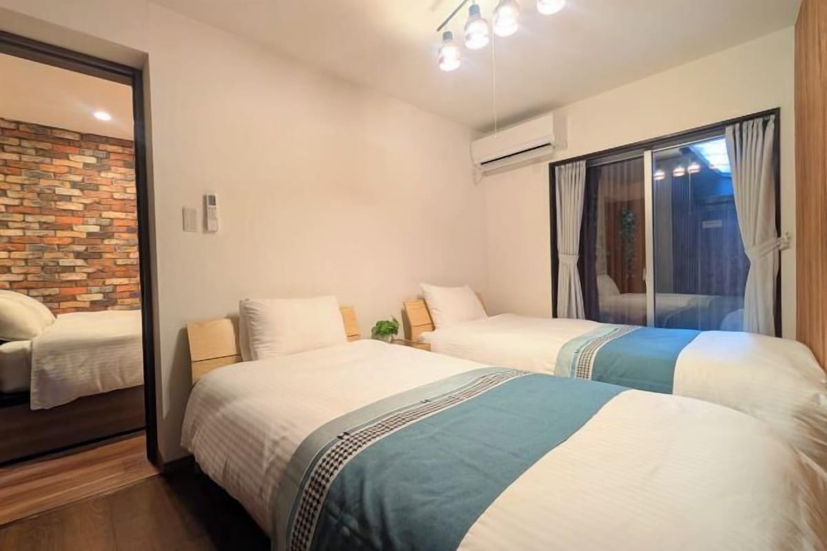 A hotel room with two beds, a brick accent wall, and a large window with curtains.