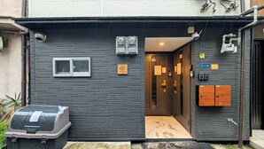 A building with a dark exterior, a window, a trash bin, and a door leading to an interior. - The Dream Stays ShinSekai (Osaka)