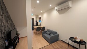 A modern living room with a grey sofa, a small table with a tissue box, and a TV on a stand. - The Dream Stays ShinSekai (Osaka)