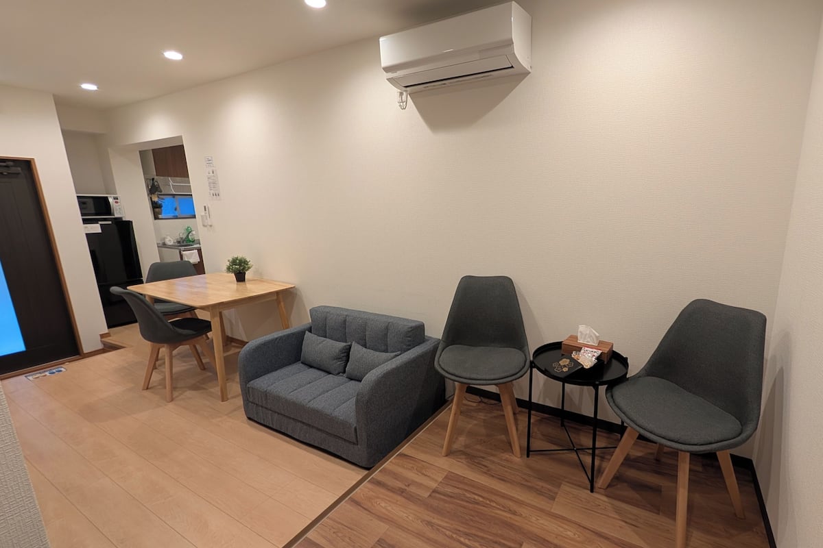 Un espacio habitable compacto con sofá, dos sillones, una mesita y una kitchenette al fondo.