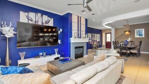Ein Wohnzimmer mit großem Flachbildfernseher, Kamin, Essbereich mit Chandelier und einer Treppe.