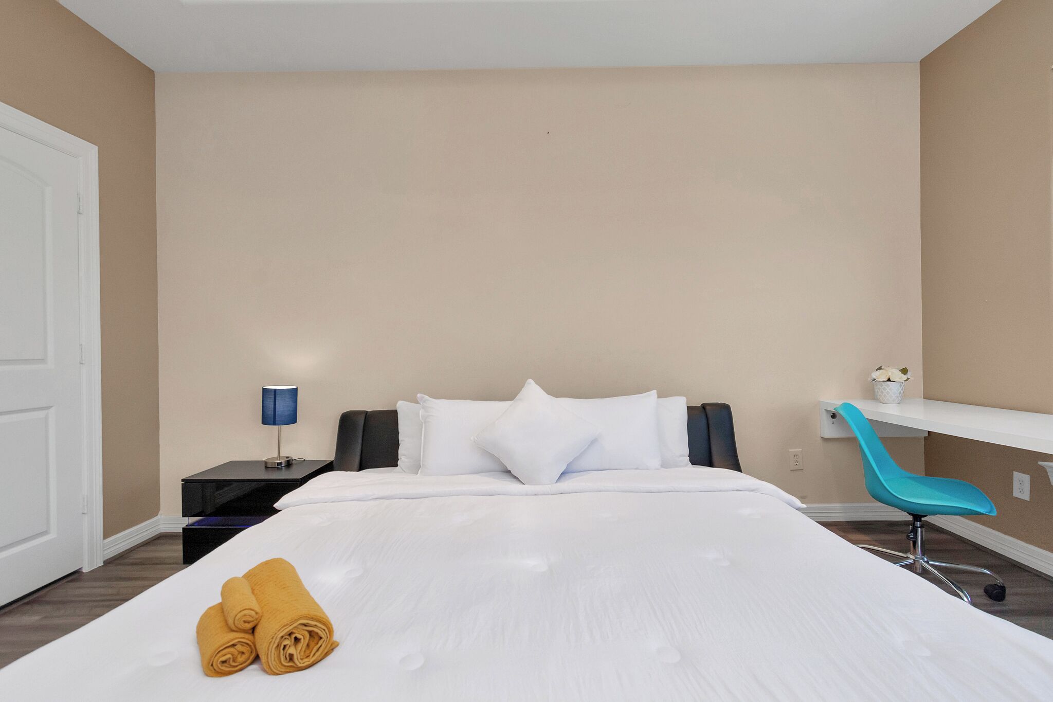 A hotel room with a bed, a nightstand with a lamp, a chair, and a small table with a plant.