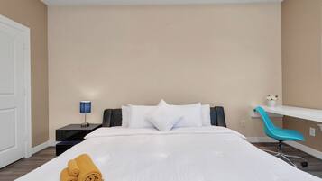 A hotel room with a bed, a nightstand with a lamp, a chair, and a small table with a plant.