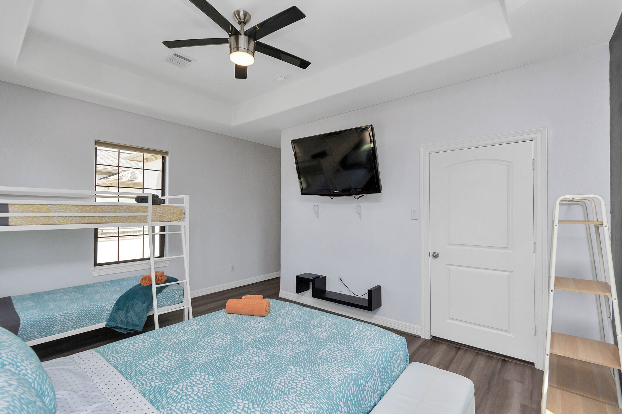A room with bunk beds, a ceiling fan, a mounted TV, a door, and a ladder.