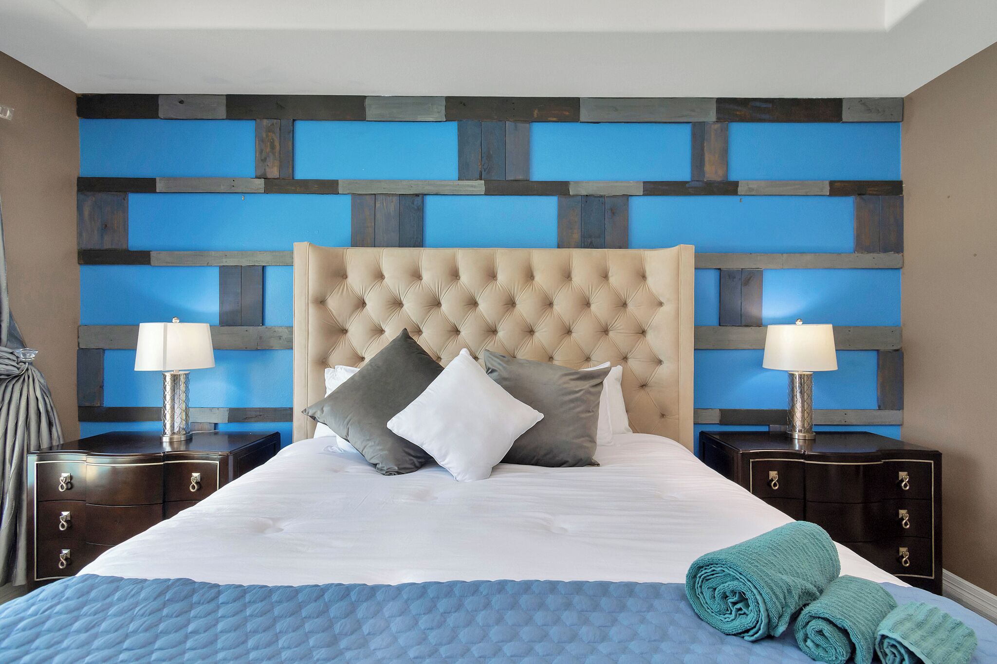 Una cama bien hecha con un cabecero capitonado, dos mesitas de noche con lámparas y una colcha azul acolchada.