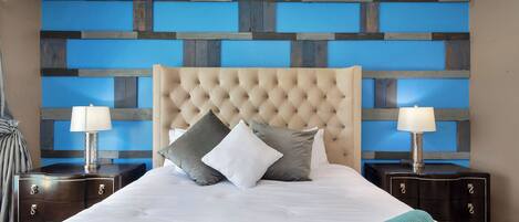 Una cama bien hecha con un cabecero capitonado, dos mesitas de noche con lámparas y una colcha azul acolchada.