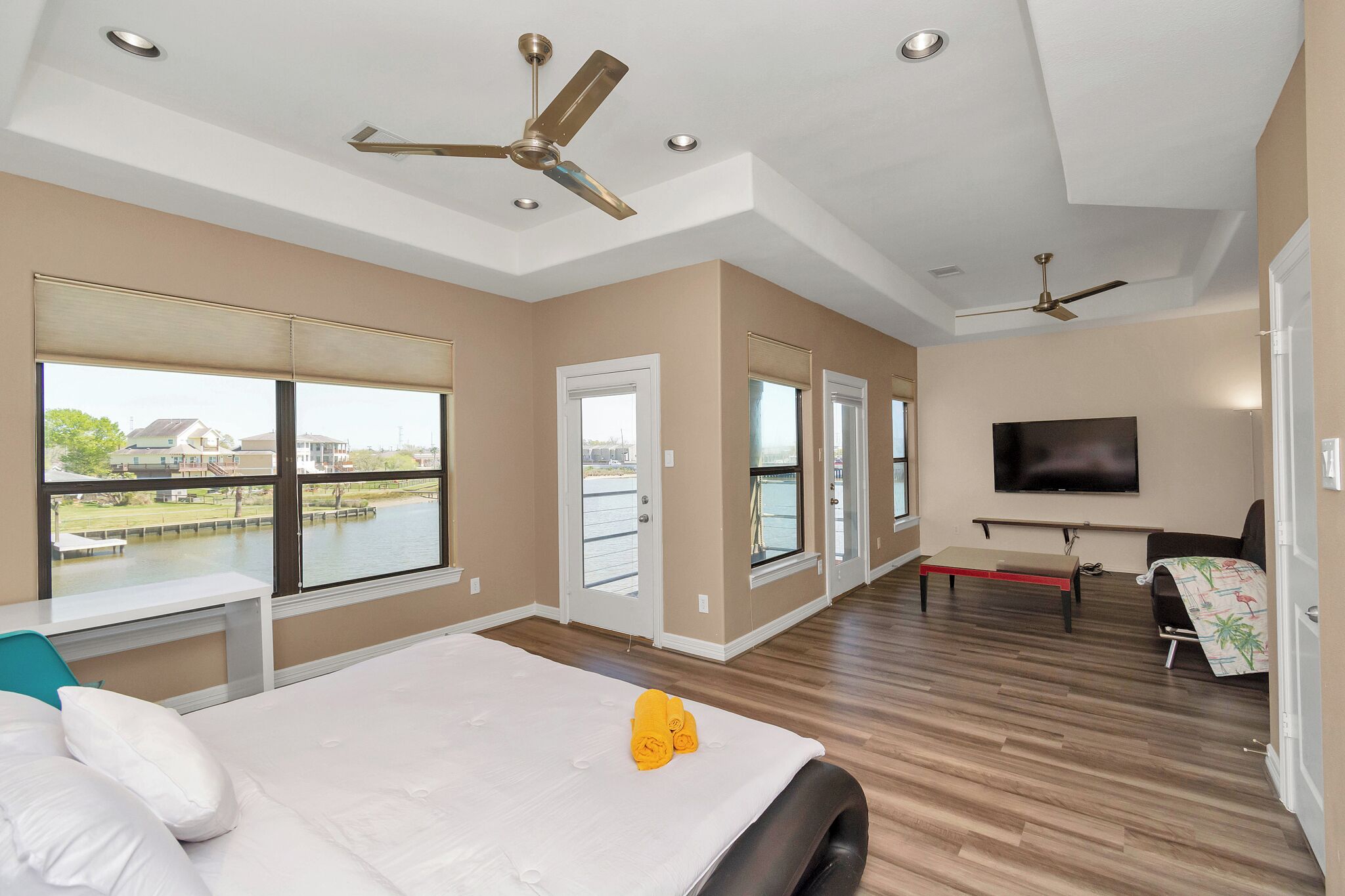 A spacious room with a large bed, a desk, a TV, and a balcony with a view of a body of water.