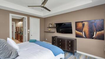 Un dormitorio con cama, ventilador de techo, televisor, cómoda y obras de arte en la pared.