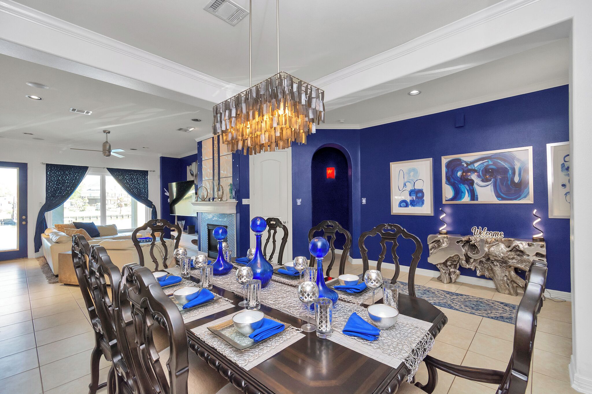 Una sala da pranzo con un lungo tavolo apparecchiato per sei persone, tovaglioli blu, posate e vasi decorativi.