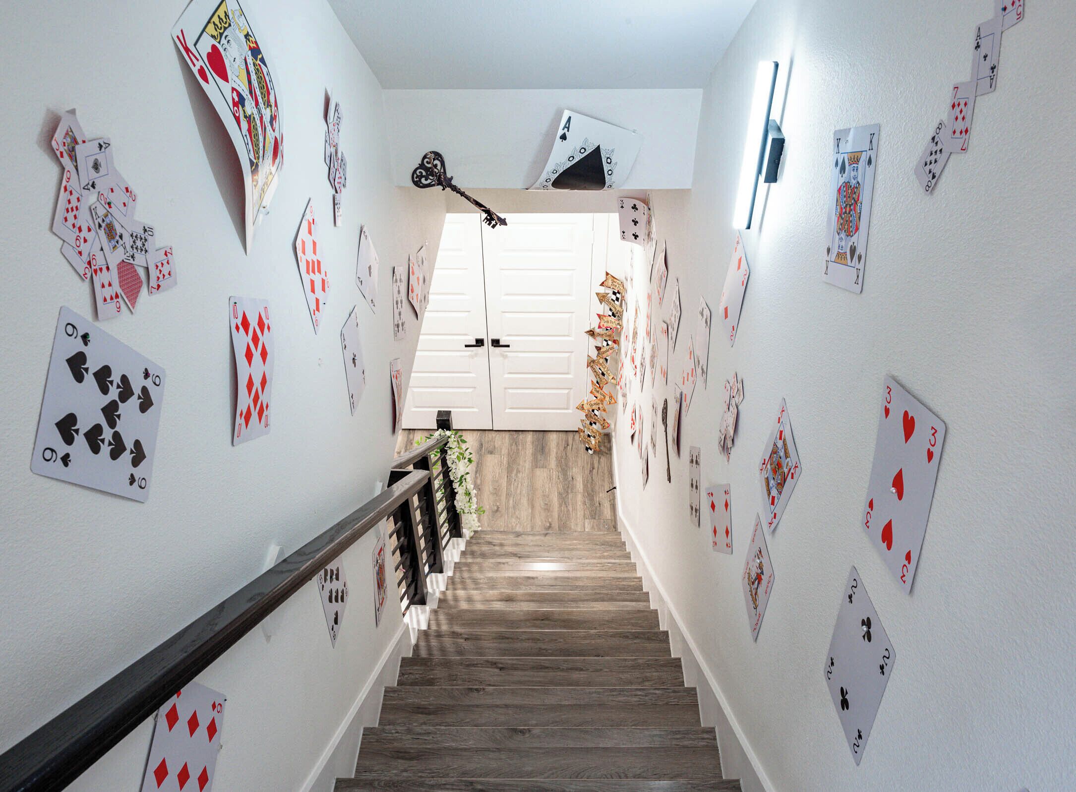 A staircase with cards on the walls, a wooden handrail, and a door at the top.