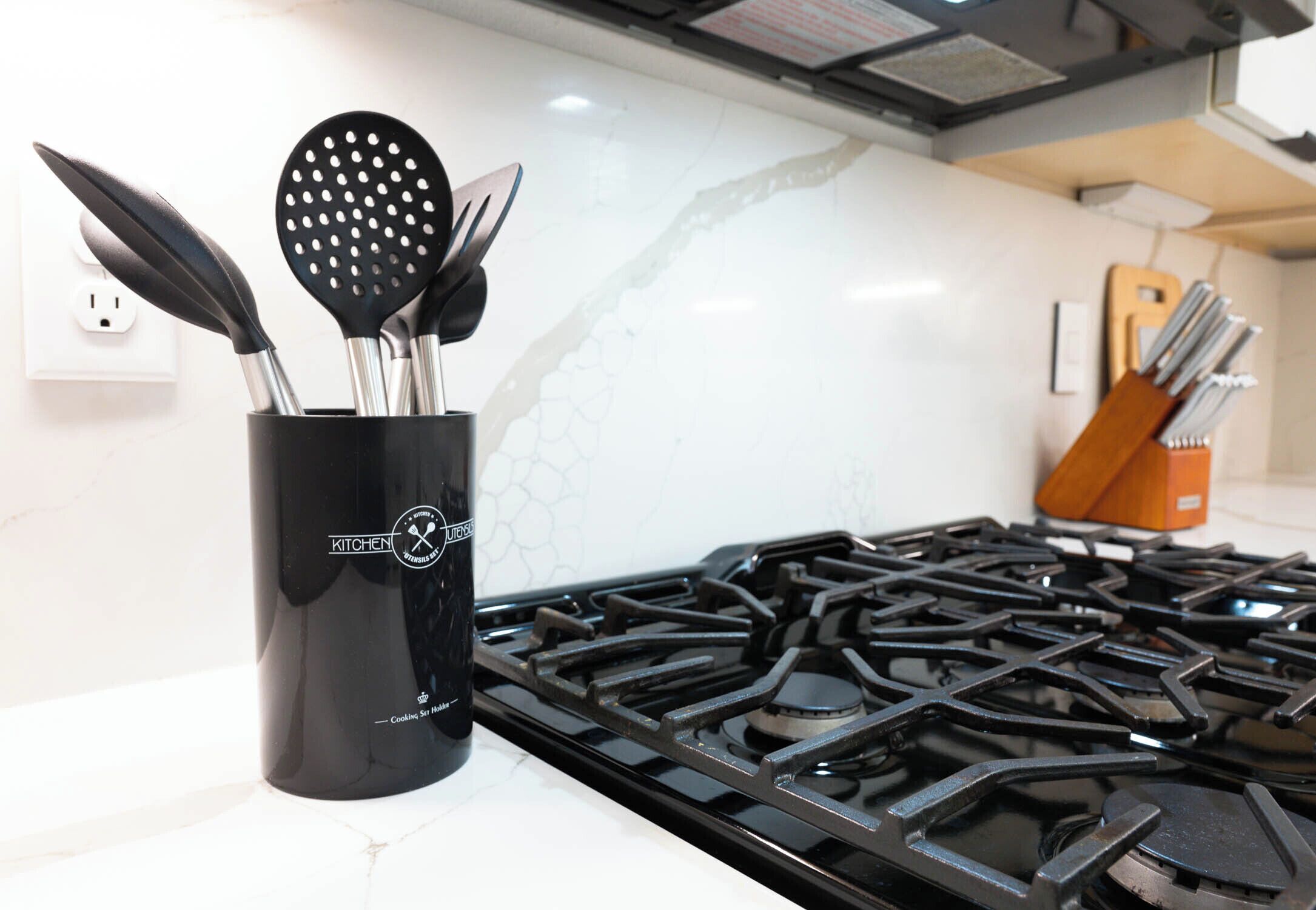 Una cocina con estufa negra, un organizador de utensilios con espátulas y un bloque para cuchillos.