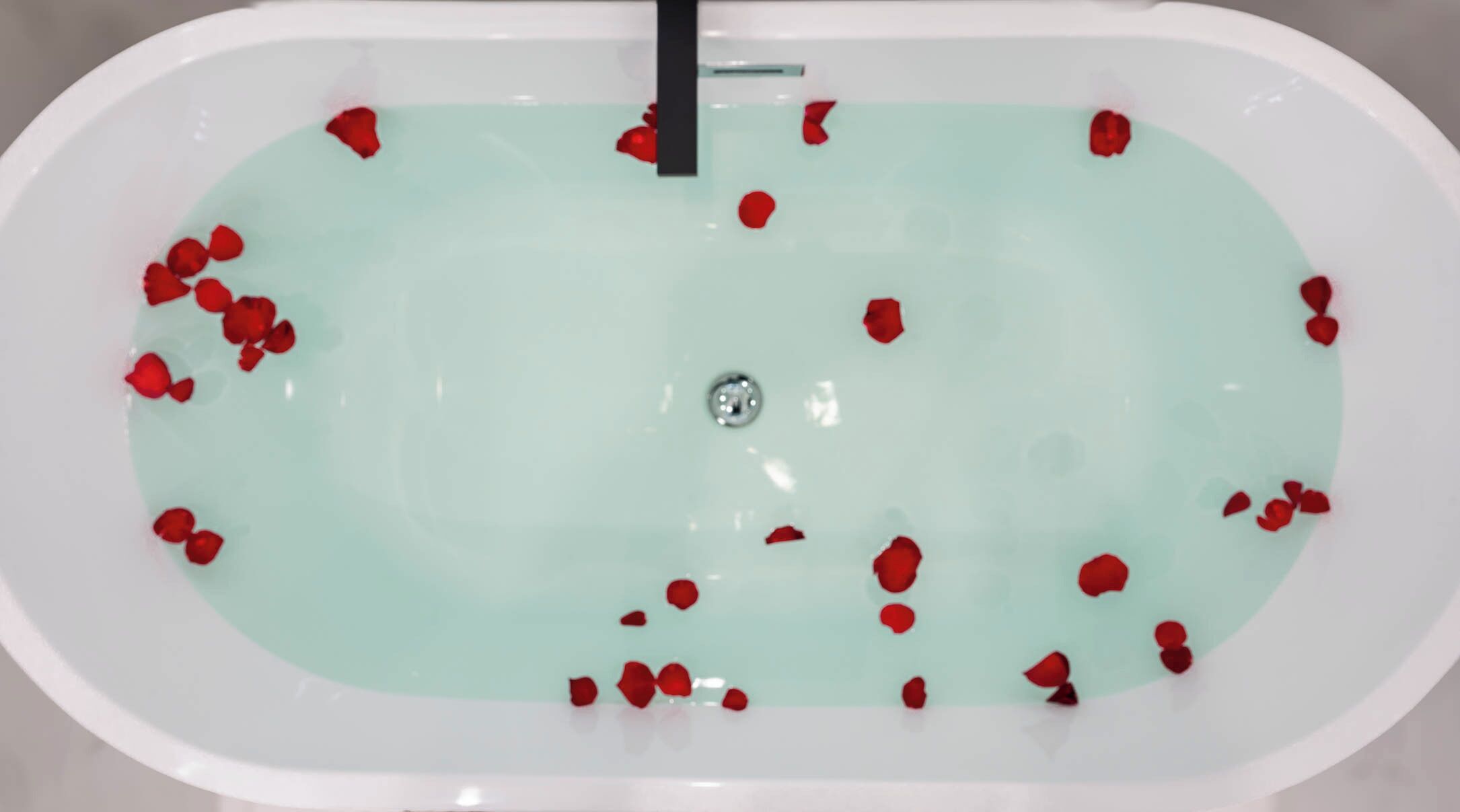 A bathtub filled with water and rose petals.