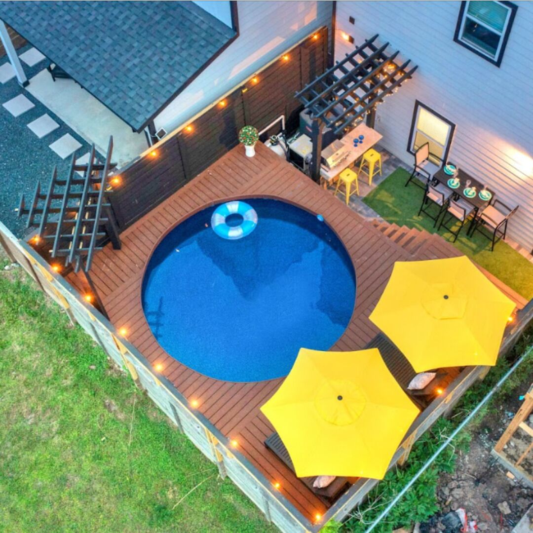 Una piscina exterior con una terraza de madera, rodeada de sombrillas amarillas y luces de cadena.