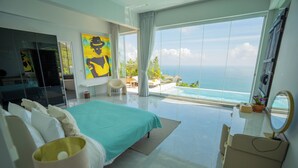 Quarto de hotel moderno com uma cama grande, TV, escrivaninha e vista para o oceano.