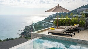 Piscina infinita no terraço com espreguiçadeiras e guarda-sol, com vista para a paisagem costeira.