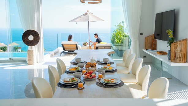Uma área de refeições com uma mesa posta para o café da manhã, um guarda-sol grande e vista para o oceano.