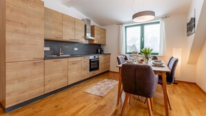 A modern kitchen with wooden cabinets, a built-in oven, and a dining area with a table and chairs. - Centrally located and at the ski slope. (Hohentauern)