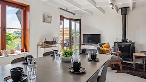 A modern living room with a large table set for dining, a television, and a wood-burning stove.