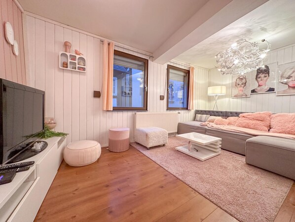 A modern living room with a flat-screen TV, a sofa, ottomans, a coffee table, and a chandelier. - Cosy, complete house in the centre of Cochem (Cochem)