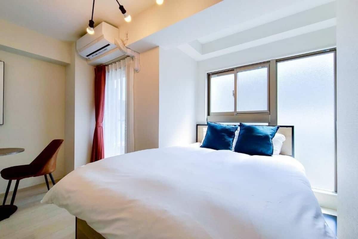 A hotel room with a large bed, a desk, a chair, an air conditioning unit, and a window.