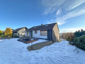 Una casa residencial amb un pati cobert de neu, una terrassa de fusta i un cel blau clar.