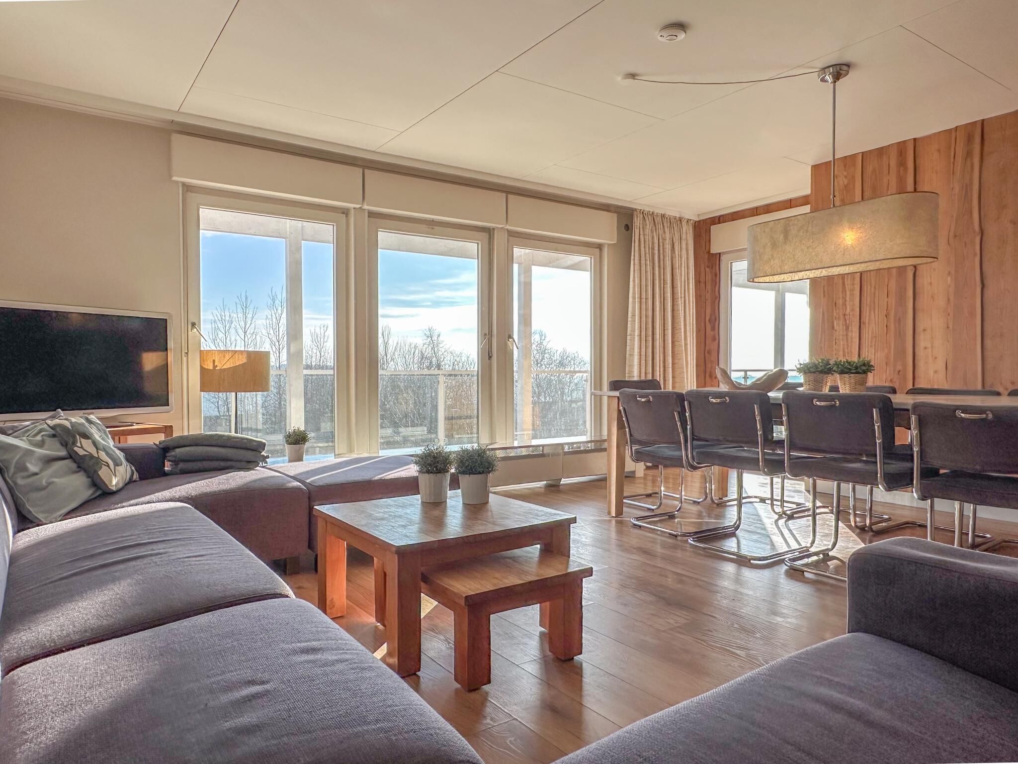 Een moderne woonkamer met een grote bank, een houten salontafel, een televisie en een eethoek met stoelen en een tafel.
