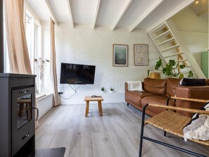 A living room with a TV, a sofa, a small table, and a staircase. - Scandinavian holiday home with a large garden (Warmenhuizen)