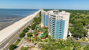 A high-rise hotel with multiple balconies, a swimming pool, and a beach view.