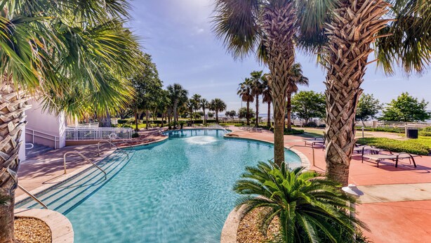A swimming pool surrounded by palm trees and a white fence. - Legacy Tower II- #1406 - 2BR/2BA Penthouse Gulf-View Condo - Resort Pools + Spa (Gulfport)
