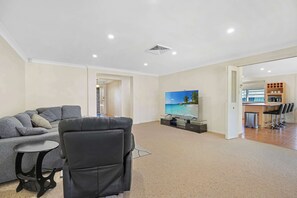 A modern living room with a sofa, a black armchair, a small round table, and a flat-screen TV.