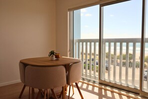 A room with a large window, a round table with chairs, a small plant, and a glass of drink.