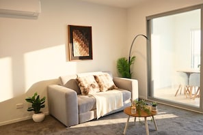 A living room with a sofa, a coffee table, a plant, and a large window.