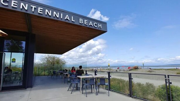 Ein Restaurant am Wasser mit dem Namen 'CENTENNIAL BEACH', das Außenplätze und einen Blick auf den Strand bietet.