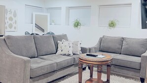 Ein Wohnzimmer mit grauem Sofa, einem runden Holztisch und einem flauschigen weißen Teppich.