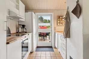 A narrow kitchen with a wooden ceiling, a coffee machine, and a view through a glass door to an outdoor seating area. - Fijne vakantiebasis bij strand en Spodsbjerg (Rudkøbing)