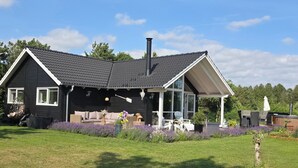 A house with a black exterior, a sloped roof, a chimney, and a covered porch with outdoor furniture.