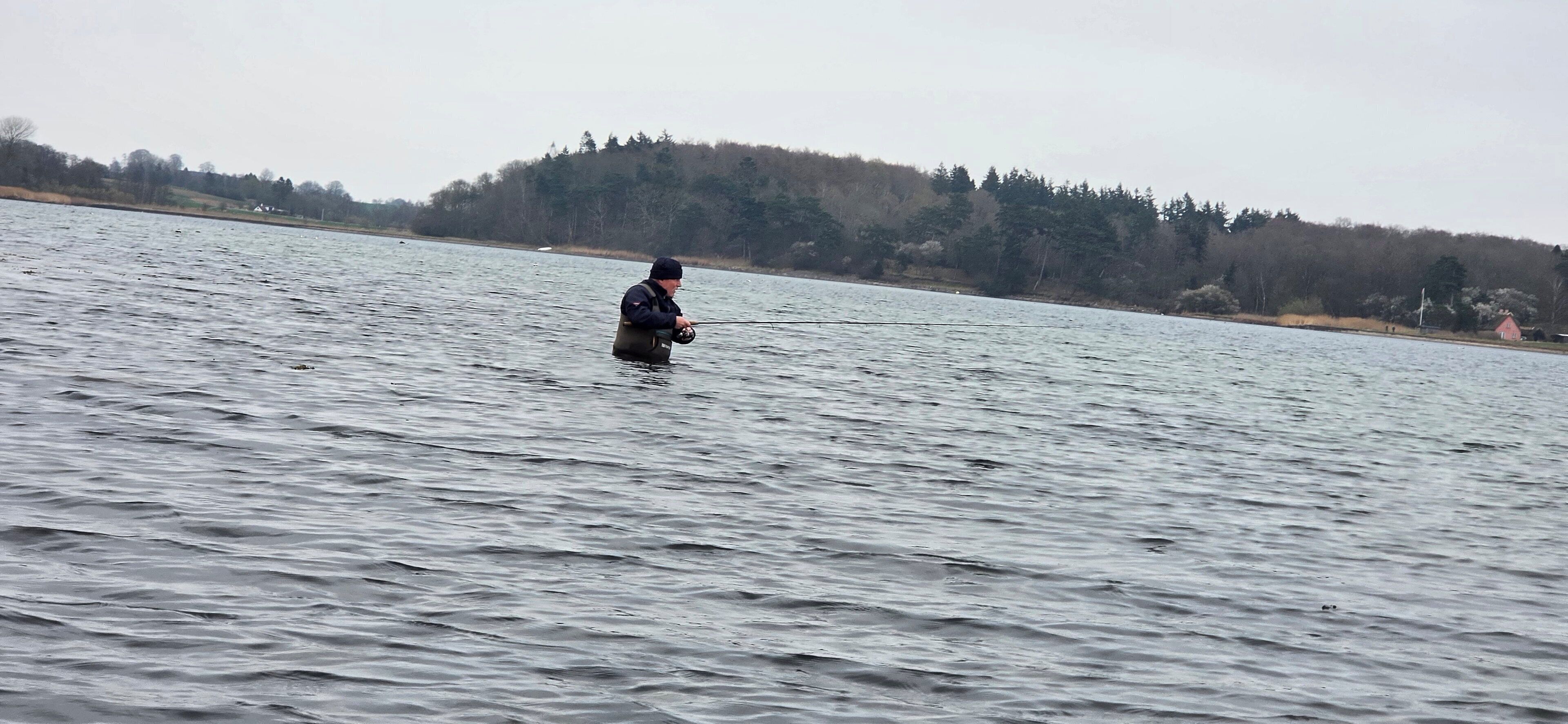 A person wading in a large body of water, holding a fishing rod.