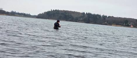 A person wading in a large body of water, holding a fishing rod.