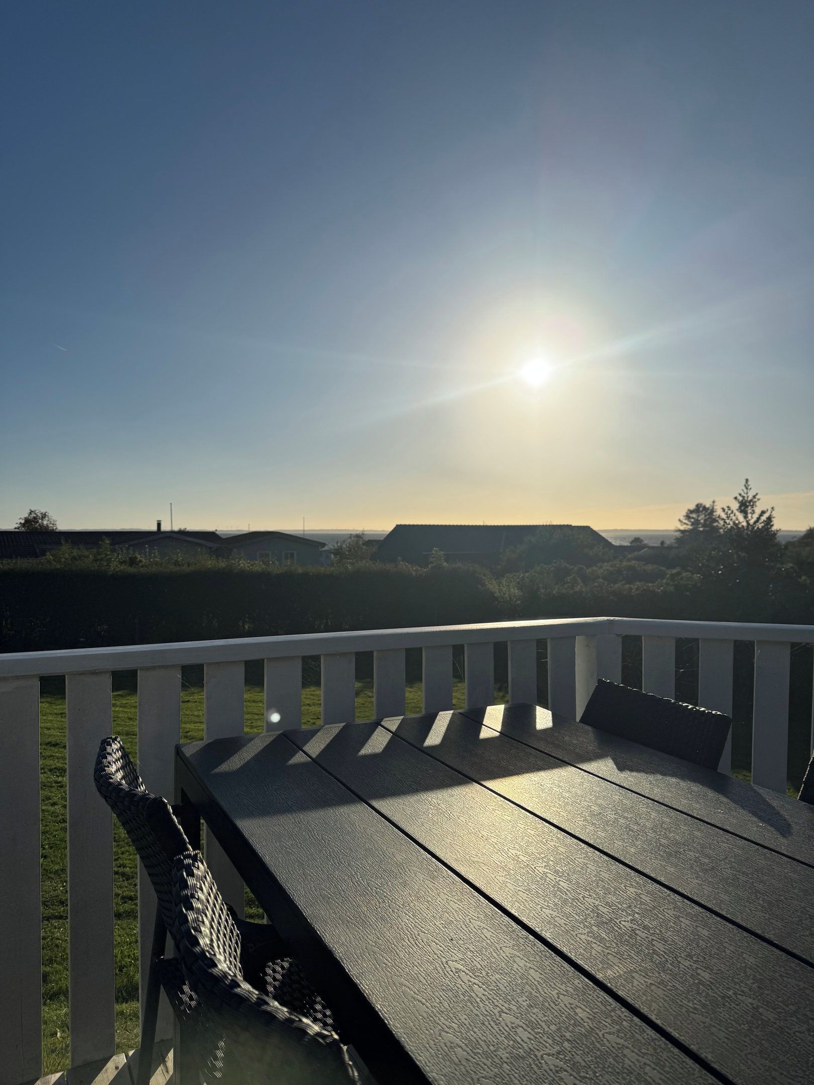 A deck with a table and chairs, overlooking a landscape with distant buildings and a clear sky.