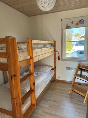 A bunk bed room with a window, wooden floor, and a small table.