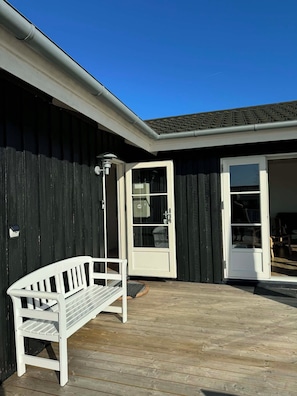 A wooden deck with a white bench, a door leading to a room, and a window. - Lovely holiday home with beautiful views (Sydals)