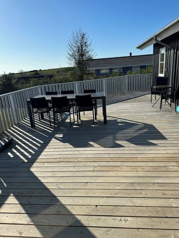 Une terrasse en bois avec une balustrade blanche, une table avec des chaises et un bâtiment en arrière-plan.