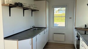 Moderni keittiö, jossa on valkoiset kaapit, musta työtaso ja ikkuna, josta avautuu näkymä vehreään maisemaan.