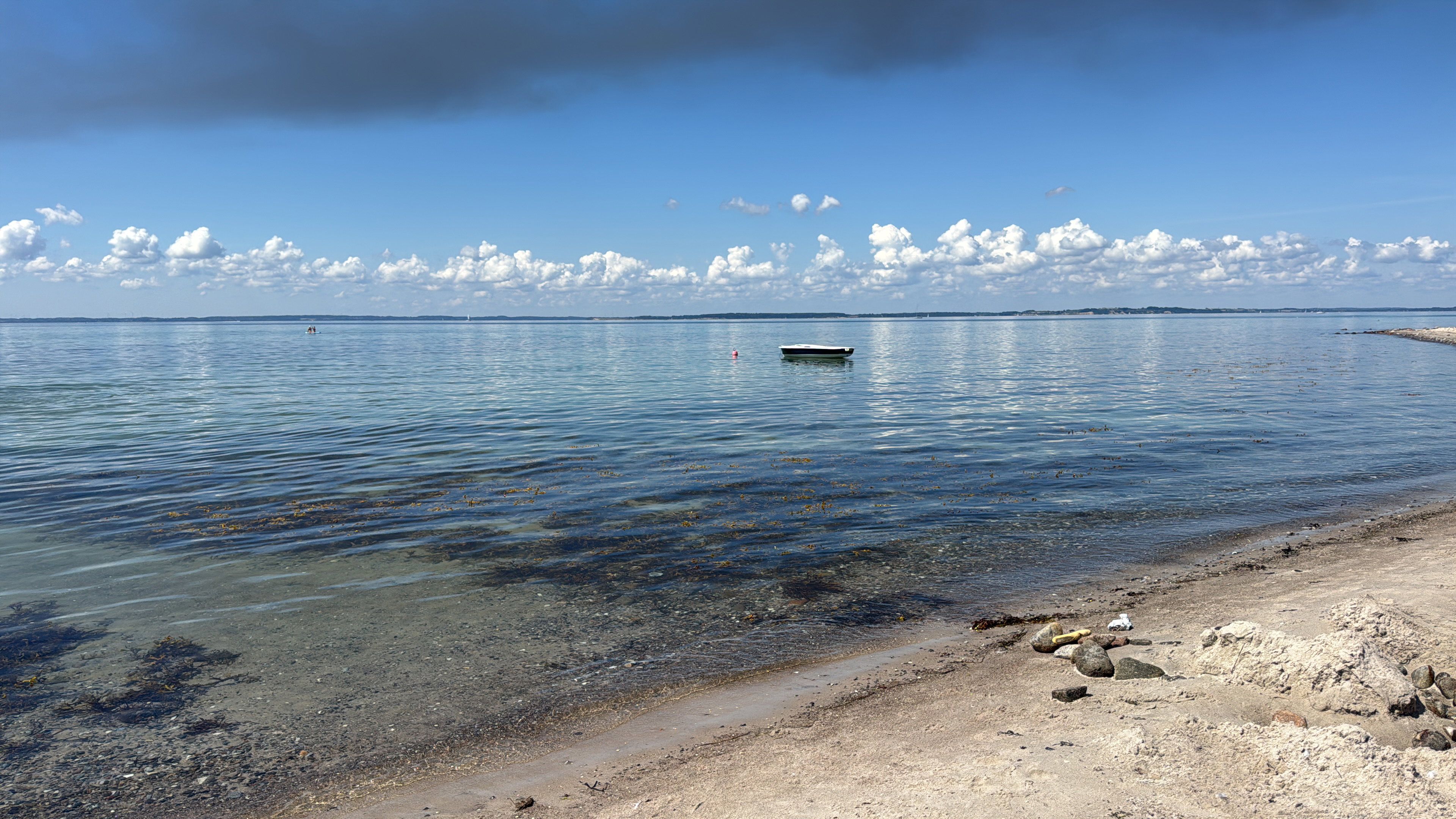 A beach with clear water, a boat, and a distant shoreline.