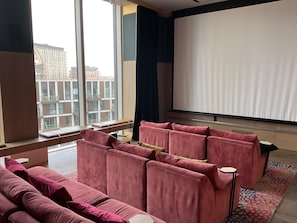 Un salón moderno con un ventanal grande, un conjunto de sofá rosa y una pantalla de proyector.