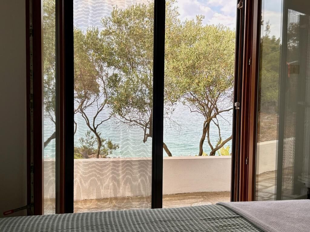 A room with a large window, a bed, and a view of trees and water.