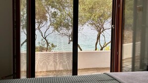 A room with a large window, a bed, and a view of trees and water. - The Coastal Garden Residence (Vourvourou)