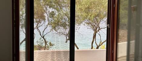 A room with a large window, a bed, and a view of trees and water.