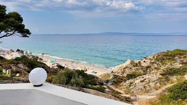 A coastal view with a beach, rocky terrain, and a clear sky. - The Coastal Garden Residence (Vourvourou)
