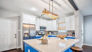 A modern kitchen with white cabinets, a central island, and a stainless steel refrigerator. - Empress Garden Villa (Houston)